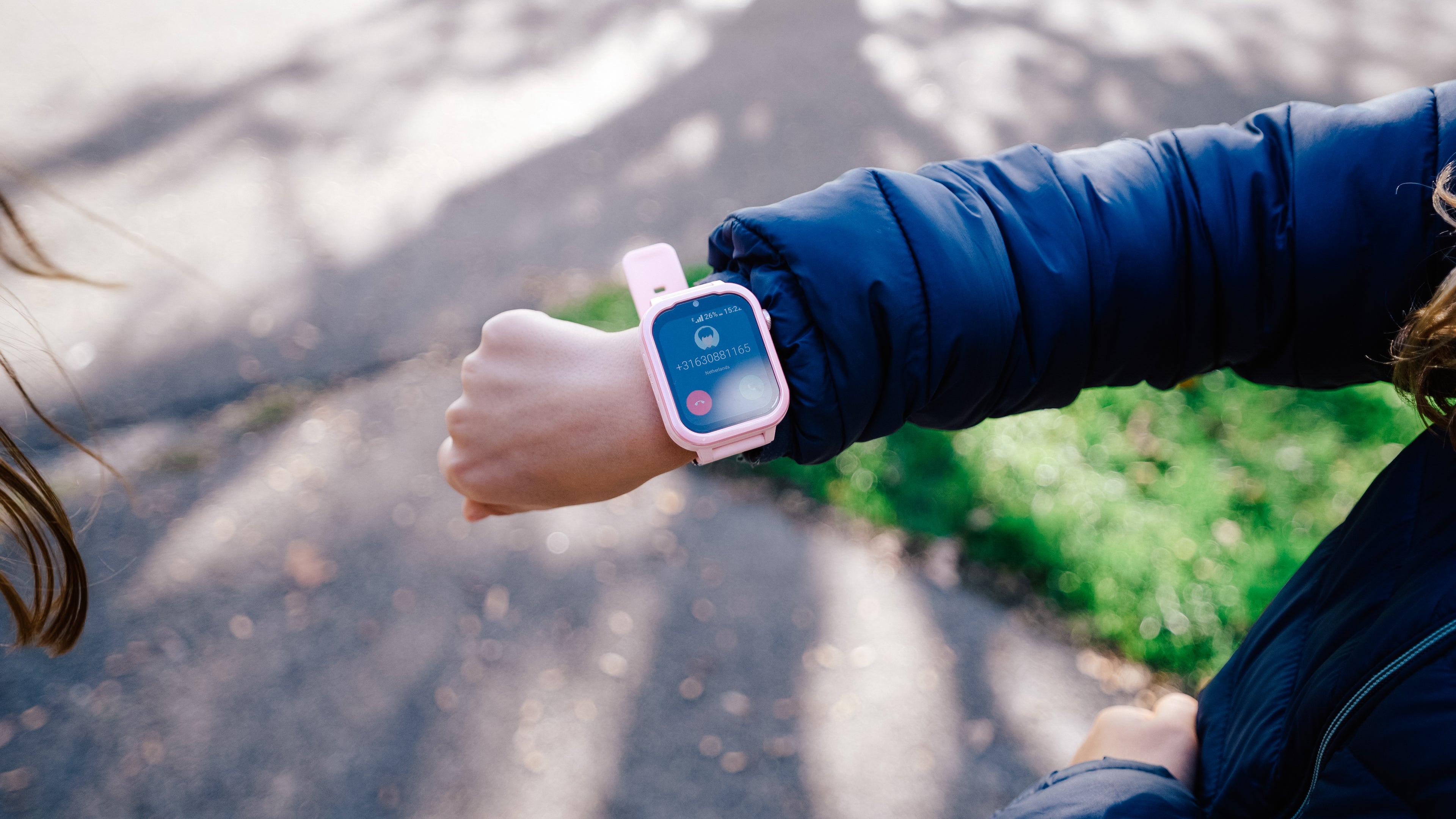 Een arm zichtbaar met een roze GPS horloge kind die aan het bellen is.